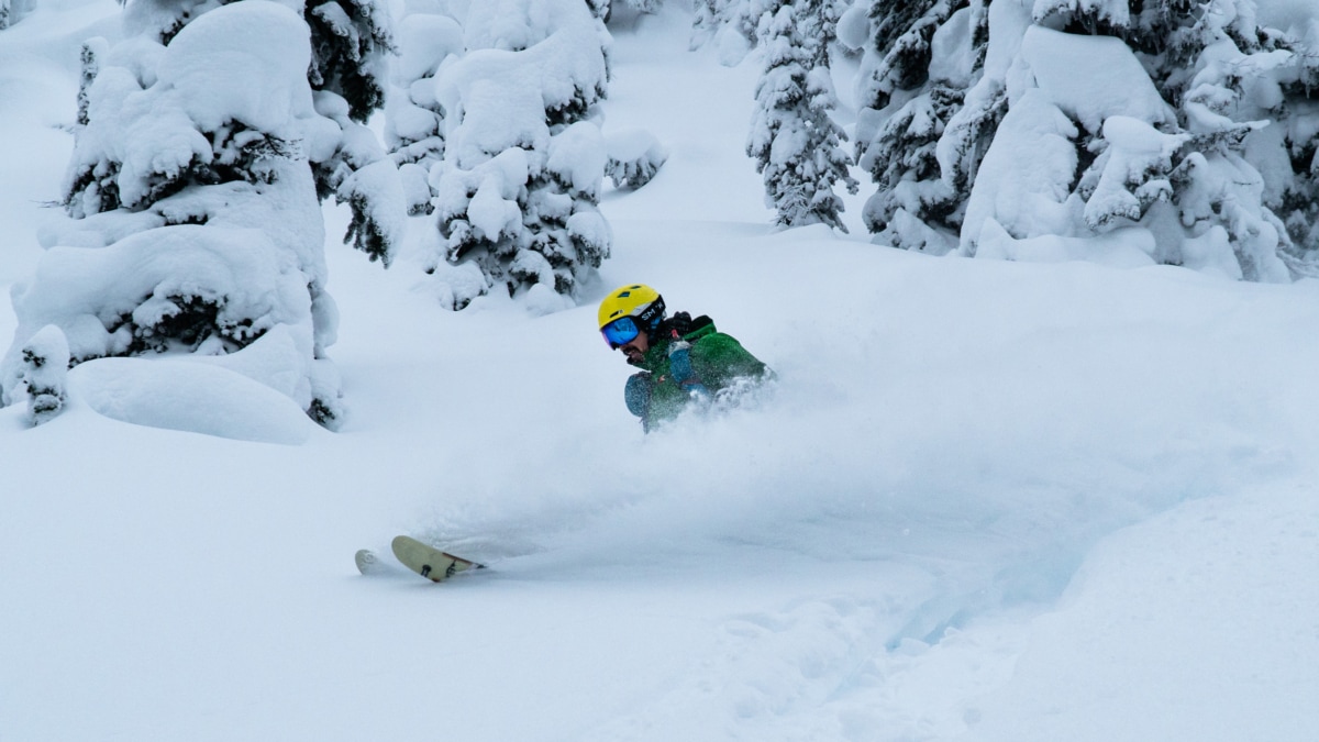 skier slashing a turn in deep powder in glades