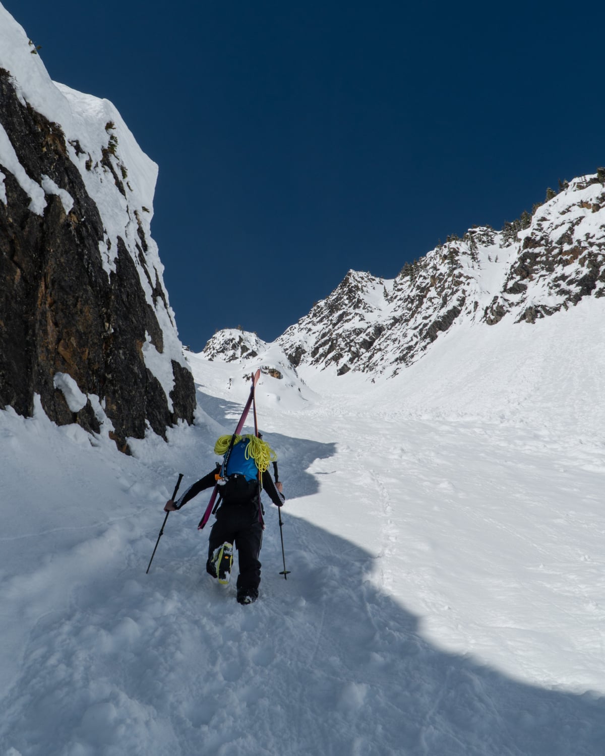 man with crampons walking up a couloir half in the sun and half in the shadow