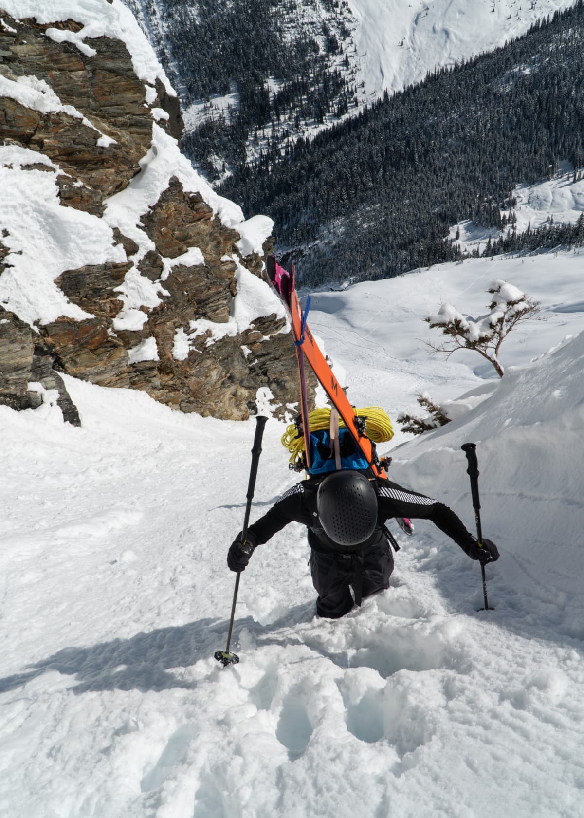 mountaineer booting up a steep couloir with skis on his back
