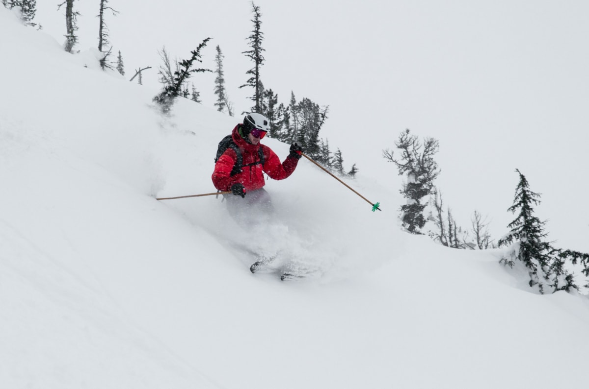 skier dressed in red slashing a turn in powder