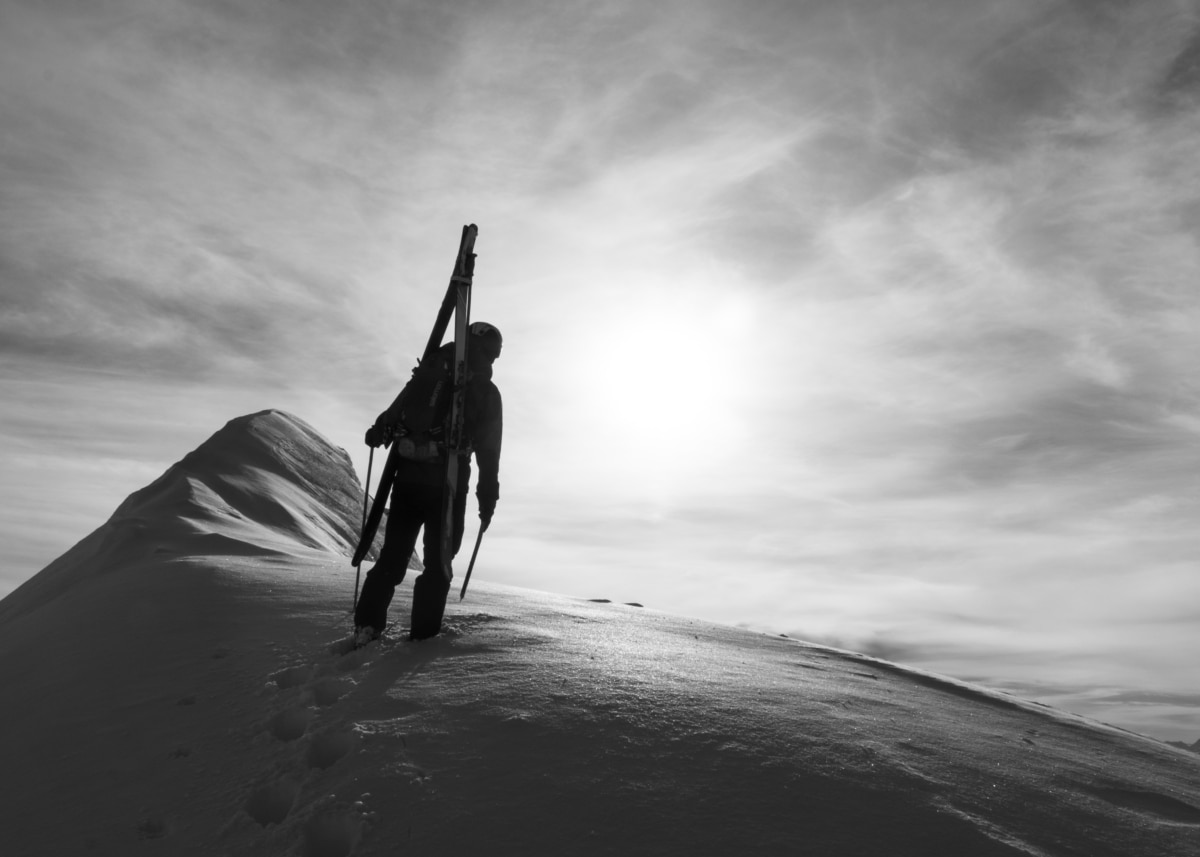 black and white shot of a man standing in front of the sun after climbing the east ridge of catamount peak